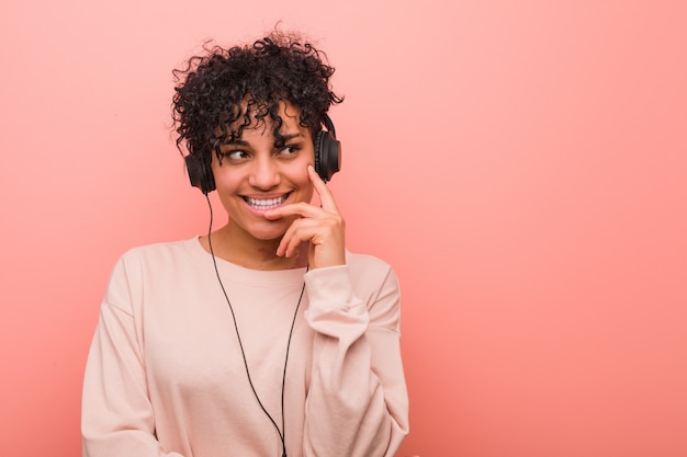 La giovane donna afroamericana che ascolta la musica si è rilassata pensando a qualcosa che esamina uno spazio della copia.