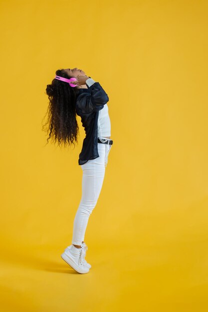 Young african american woman listening to music with headphones doing a tiptoe