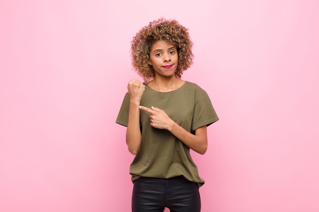 Young african american woman looking impatient and angry, pointing at watch, asking for punctuality, wants to be on time against pink wall