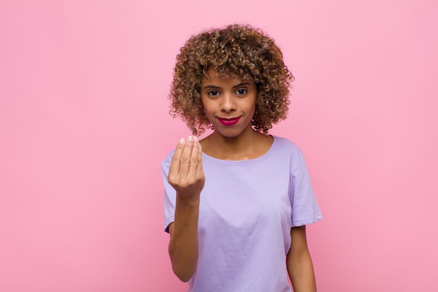 Giovane donna afroamericana che fa capice o gesto di denaro, che ti dice di pagare i tuoi debiti! contro il muro rosa