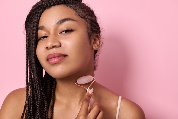 Young african american woman massaging her neck, using jade
roller stone massager. close-up