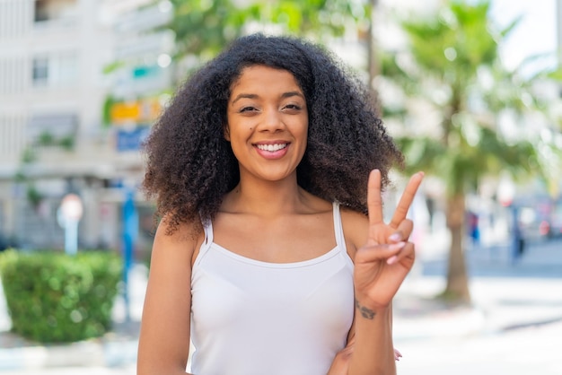 アフリカ系アメリカ人の若い女性が外で笑顔で勝利のサインを示しています