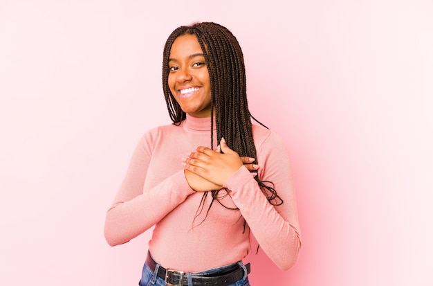 Young african american woman on a pink has friendly expression, pressing palm to chest. Love concept.