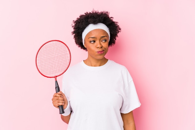 Young african american woman playing badminton isolated confused, feels doubtful and unsure.