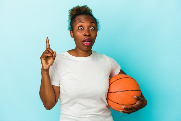 Молодая афро-американская женщина играет в баскетбол, изолированные на синем фоне, имея идею, концепцию вдохновения.