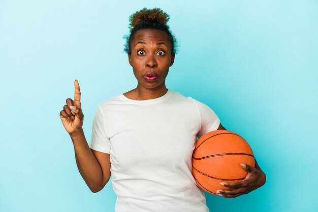 Young african american woman playing basketball isolated on blue background having some great idea, concept of creativity.