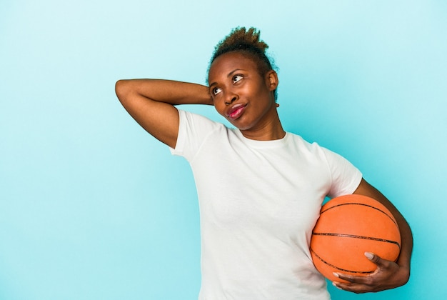 Giovane donna afroamericana che gioca a basket isolata su sfondo blu toccando la parte posteriore della testa, pensando e facendo una scelta.