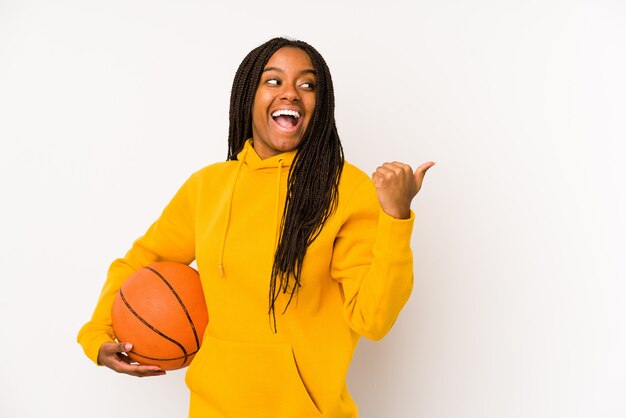 Young african american woman playing basketball isolated points with thumb finger away, laughing and carefree.