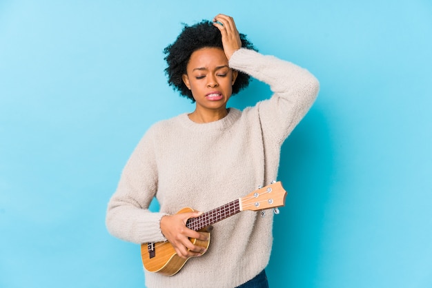 Young african american woman playing ukelele isolated being shocked, she has remembered important meeting.