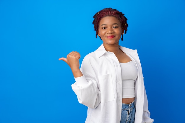 Young african american woman pointing to copy space against blue