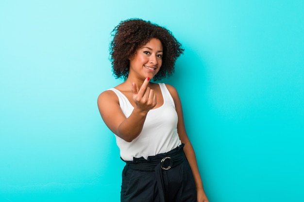 Young african american woman pointing with finger at you as if inviting come closer.