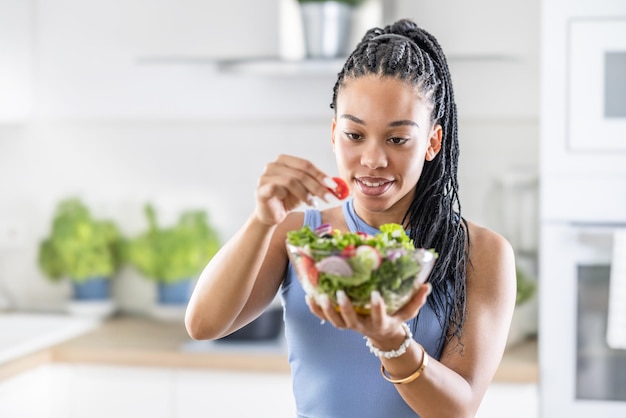 Foto la giovane donna afroamericana prepara un'insalata sana e aggiunge pomodori