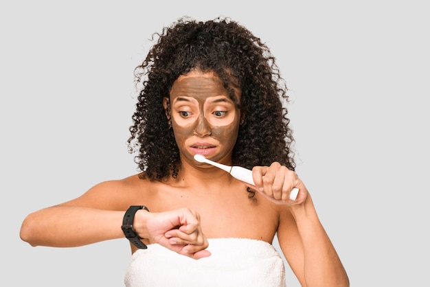 Young african american woman preparing to go out for dinner brushing her teeth looking at the time on the clock