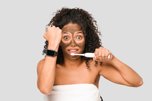 Young african american woman preparing to go out for dinner brushing her teeth looking at the time