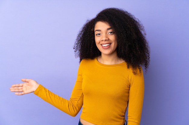 Young african american woman on purple wall extending hands to the side