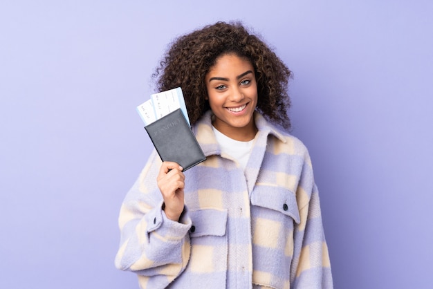 Молодая Афро-американская женщина на фиолетовой стене счастливая в каникулах с паспортом и билетами на самолет