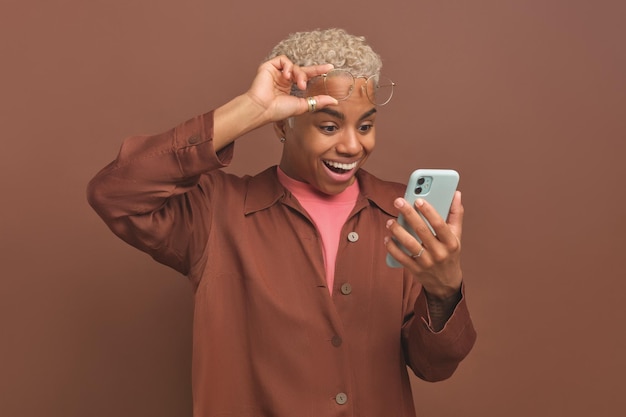 Young african american woman raises glasses from eyes looking at smartphone