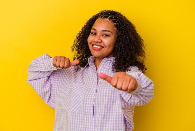 若いアフリカ系アメリカ人の女性は、笑顔と自信を持って、両方の親指を上げます。