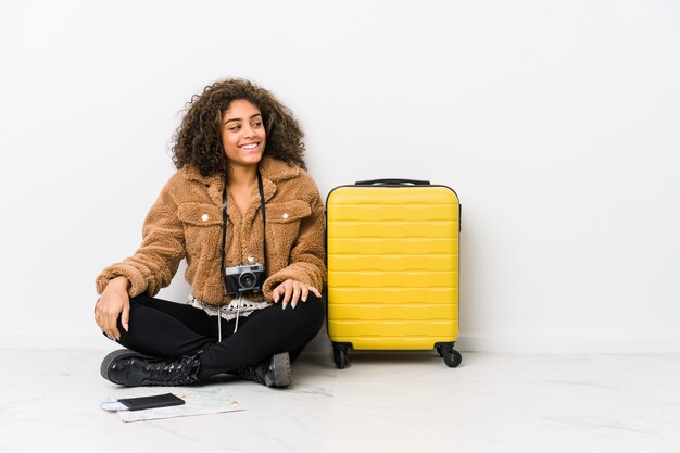 Young african american woman ready for a travel looks aside smiling, cheerful and pleasant.