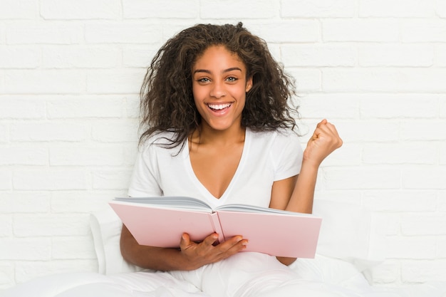 Young african american woman sitting on the bed studying cheering carefree and excited.