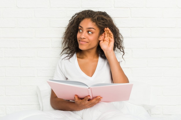 Young african american woman sitting on the bed studying trying to listening a gossip.