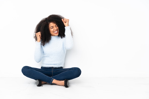 Young african american woman sitting on the floor celebrating a victory