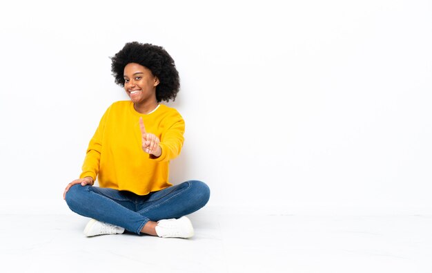 Young African American woman sitting on the floor showing and lifting a finger