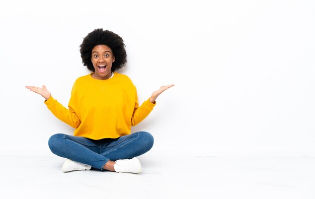 Giovane donna afro-americana seduta sul pavimento con l'espressione del viso scioccata