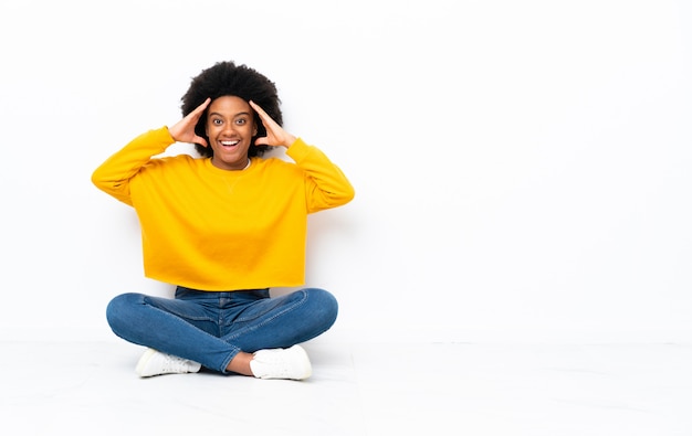 Photo young african american woman sitting on the floor with surprise expression