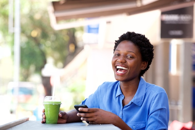 Young african american woman sitting at outdoor cafe with a mobile phone and laughing