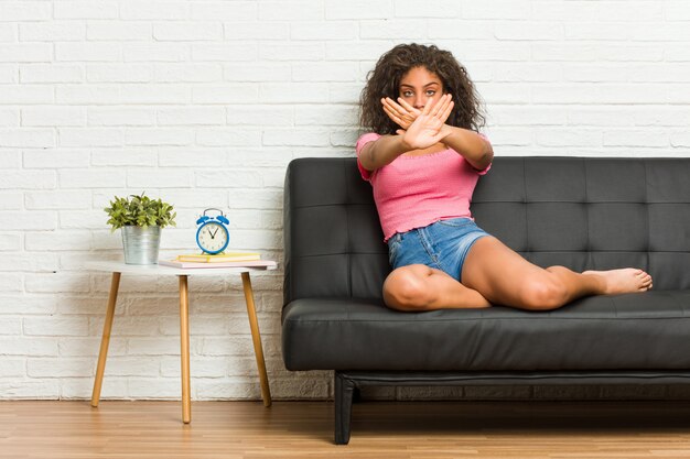 Young african american woman sitting on the sofa doing a denial gesture