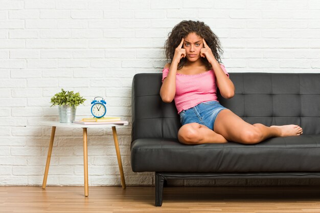 Young african american woman sitting on the sofa focused on a task, keeping forefingers pointing head