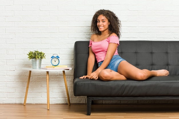 Young african american woman sitting on the sofa looks aside smiling, cheerful and pleasant.