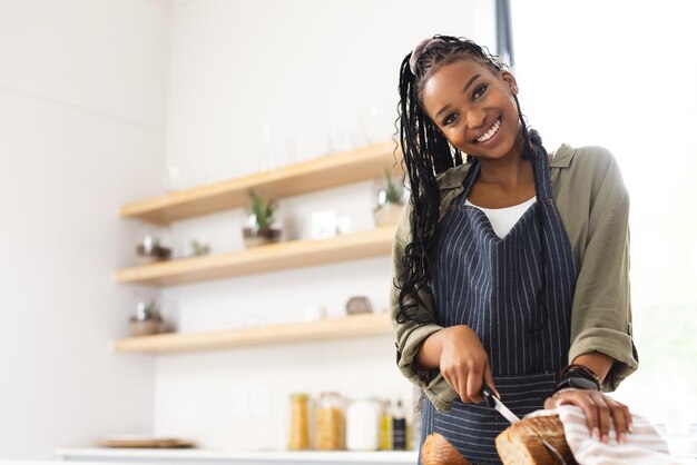 Молодая афроамериканка нарезает хлеб на светлой кухне с копировальным пространством
