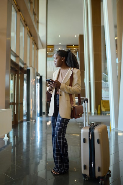 Giovane donna afroamericana in abbigliamento casual intelligente in piedi nel corridoio dell'hotel