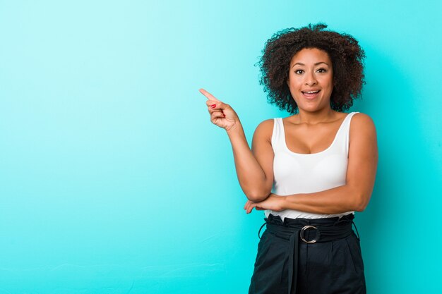 Молодая Афро-американская женщина усмехаясь жизнерадостно указывая с указательным пальцем прочь.