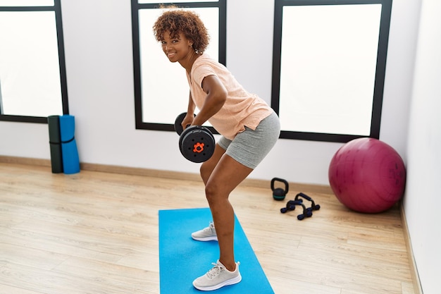 Young african american woman smiling confident training using dumbbell at sport center