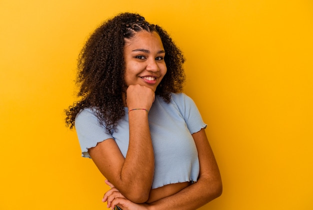 Giovane donna afroamericana sorridente felice e fiduciosa, toccando il mento con la mano.