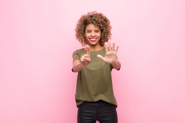 Young african american woman smiling and looking friendly, showing number six or sixth with hand forward, counting down against pink wall