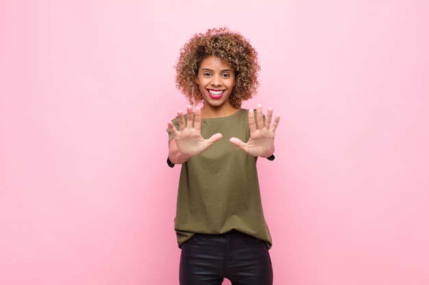 Young african american woman smiling and looking friendly, showing number ten or tenth with hand forward, counting down against pink wall