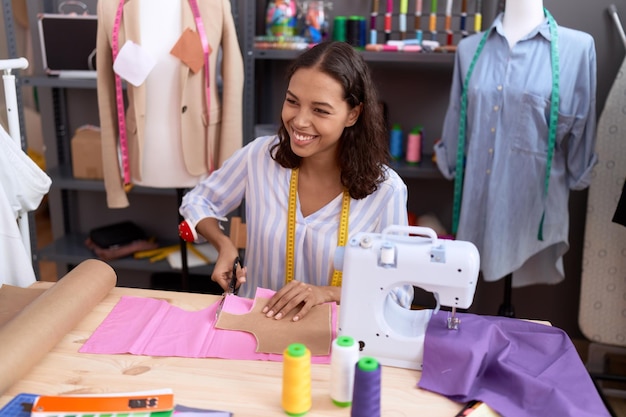 Young african american woman tailor smiling confident cutting cloth at atelier