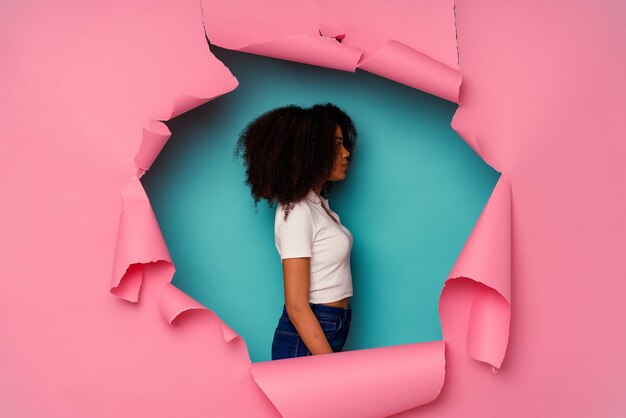 Молодая афро-американская женщина в рваной бумаге, изолированной на синем фоне, глядя влево, боком.