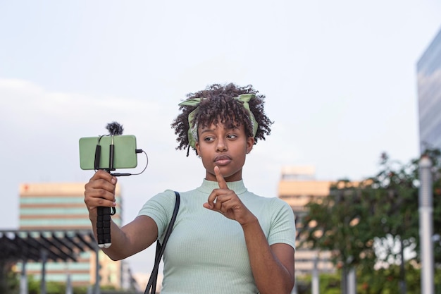 若いアフリカ系アメリカ人女性が街を歩き回り、スマートフォンで生放送をする若いブロガーのコンセプトコピースペース