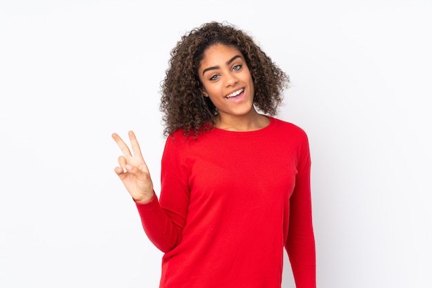 Young African American woman on wall smiling and showing victory sign