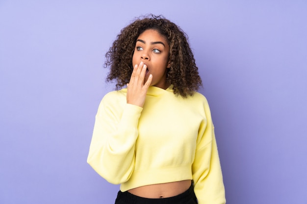 Young African American woman on wall yawning and covering wide open mouth with hand