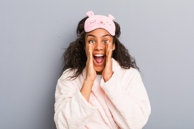 Young african american woman wearing a pajamas and a sleep mask shouting excited to front.