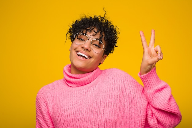 Photo young african american woman wearing a pink sweater joyful and carefree showing a peace symbol with fingers.