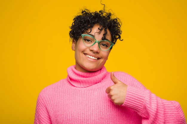 Giovane donna afroamericana che indossa un maglione rosa che sorride e che alza pollice in su