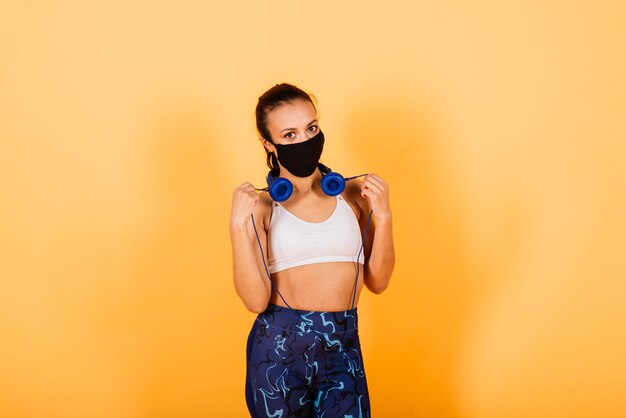 Young african american woman wearing sportswear and medical mask, celebrating victory and success very excited with raised arms, training with dumbbells