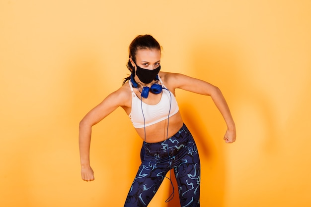 Young african american woman wearing sportswear and medical mask, celebrating victory and success very excited with raised arms, training with dumbbells